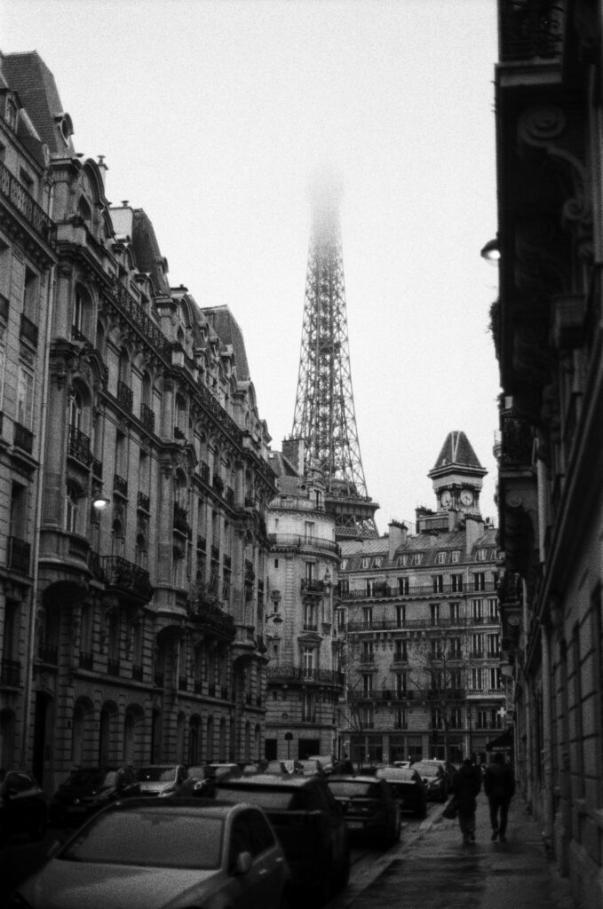 Black and white view of a Paris street with the Eiffel Tower shrouded in fog, capturing urban charm.