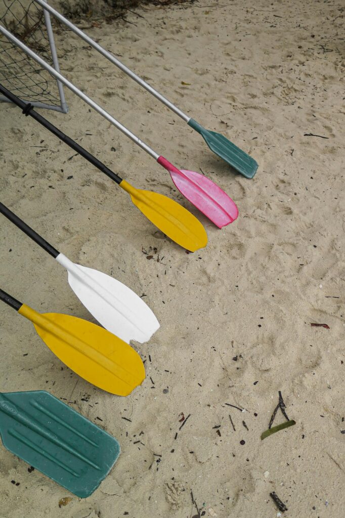 A variety of colorful paddles laid out on a sandy beach, showcasing a vibrant outdoor setting.